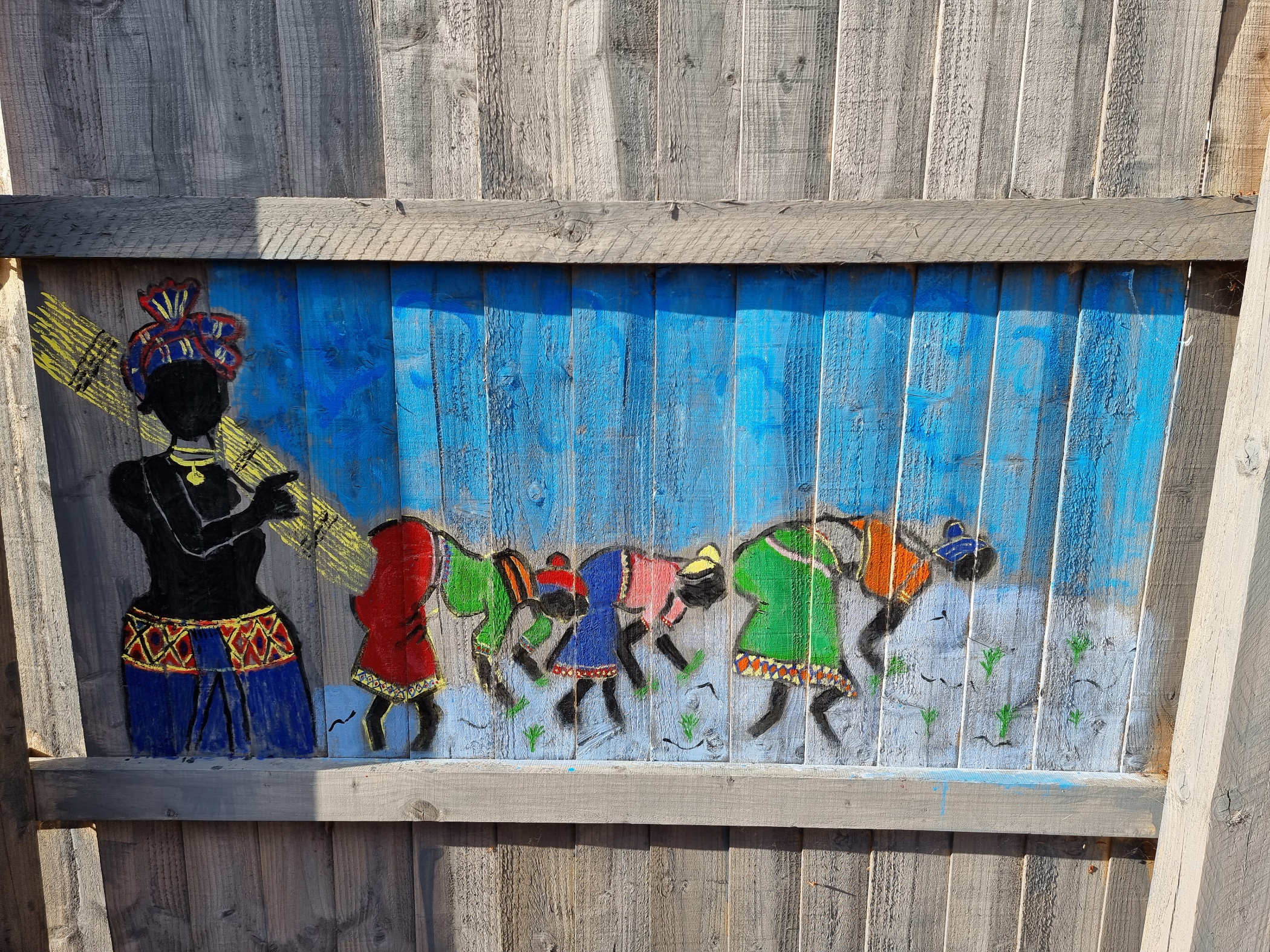 Painting by Dr Abhi on his fence. Blue background with colourful figures in a line.