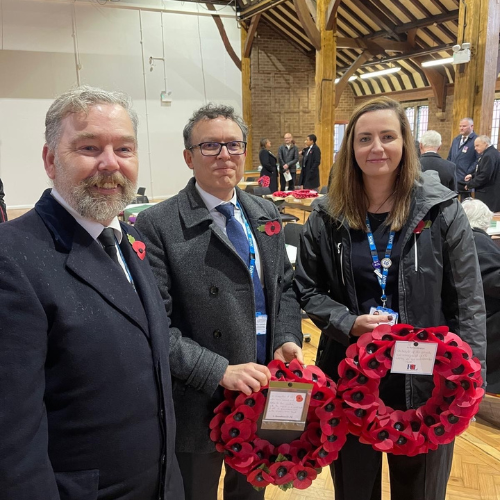 Three people stand holding two poppy wreaths