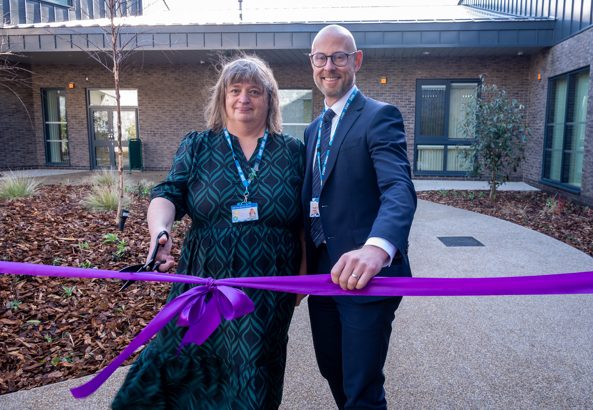 man and woman holding a purple ribbon ready to cut for the opening 