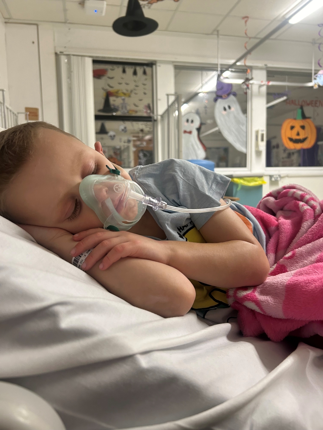 Liam in hospital asleep on a bed in an oxygen mask.jpg
